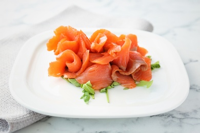 Plate with fresh sliced salmon fillet and arugula on marble table