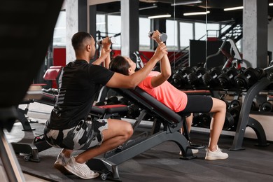 Photo of Young woman working out with professional trainer in modern gym