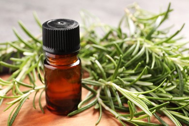 Photo of Bottle of essential oil and fresh rosemary on board, closeup