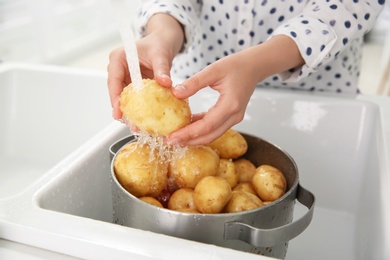 Photo of Woman washing fresh potatoes in kitchen sink, closeup
