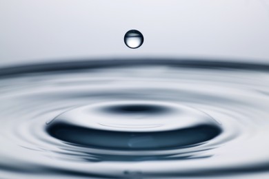 Photo of Drop falling into clear water on light grey background, closeup