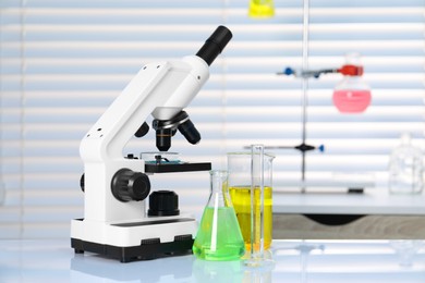 Photo of Laboratory analysis. Different glassware with liquids and microscope on white table indoors