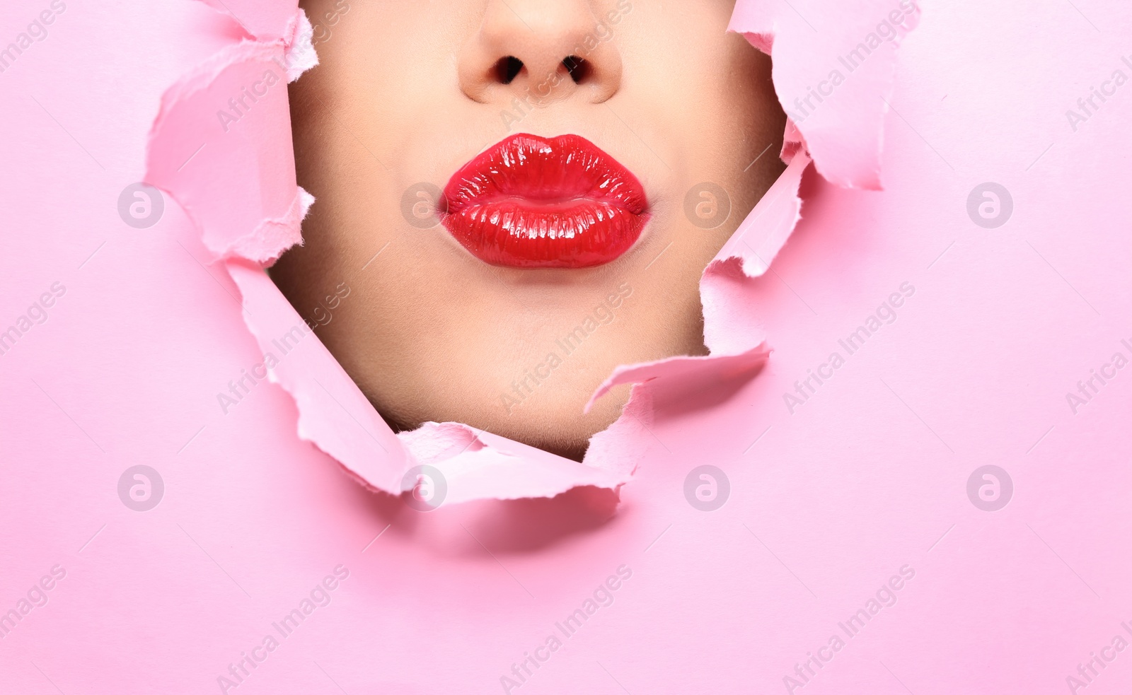 Photo of View of beautiful young woman with red lips through hole in color paper, closeup