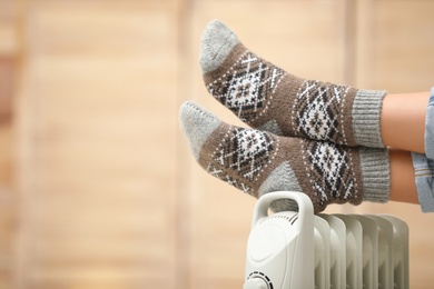 Photo of Woman warming feet on electric heater at home, closeup. Space for text