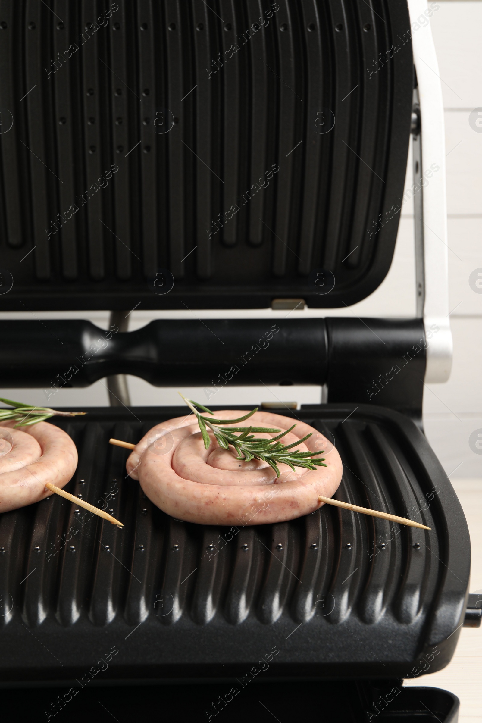 Photo of Electric grill with homemade sausages and rosemary on light background, closeup