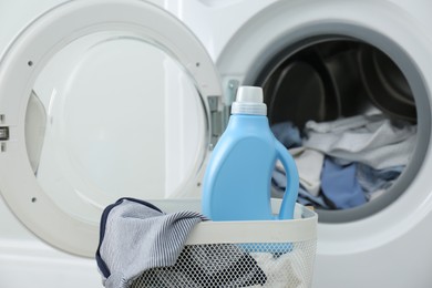 Photo of Bottle of detergent and children's clothes in basket near washing machine