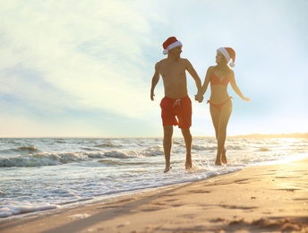 Photo of Happy couple with Santa hats together on beach. Christmas vacation