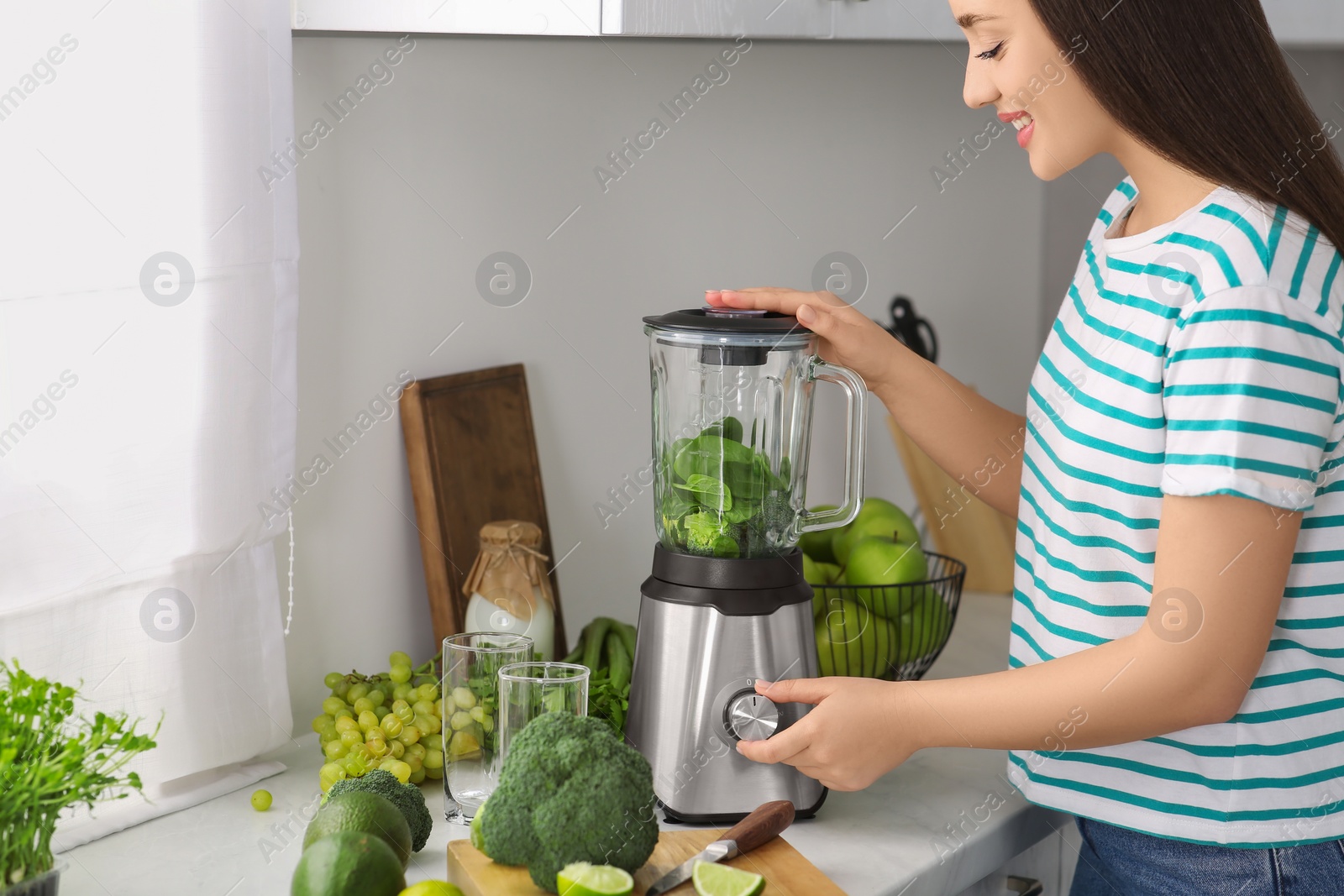 Photo of Beautiful young woman preparing tasty smoothie in kitchen