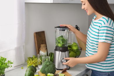 Beautiful young woman preparing tasty smoothie in kitchen