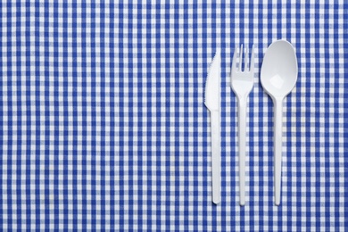 Plastic cutlery and space for text on plaid fabric, flat lay. Table setting