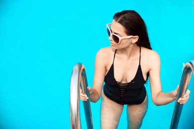 Beautiful young woman getting out of blue swimming pool