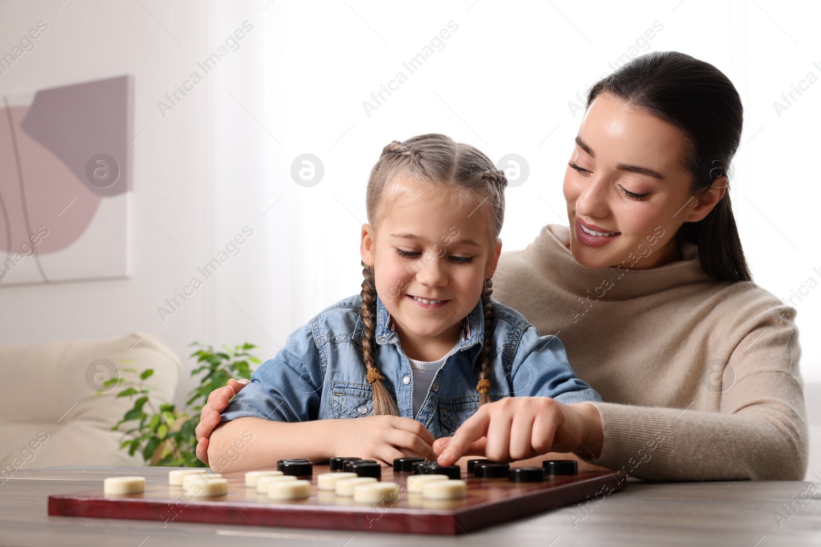 Photo of Playing checkers. Mother learning her daughter at table in room