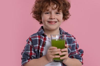 Cute little boy with glass of fresh juice on pink background