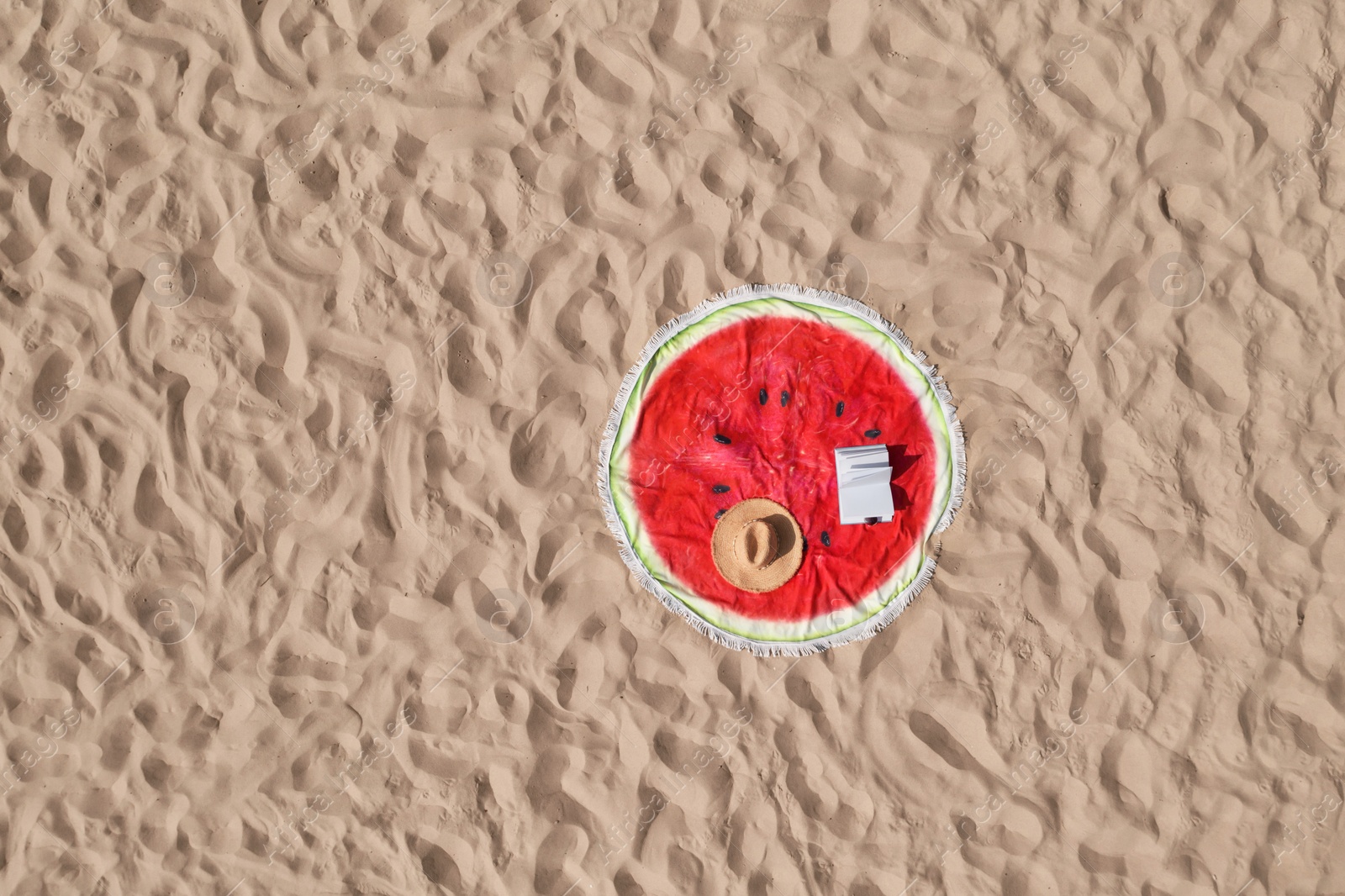 Image of Towel with book and straw hat on sandy beach, aerial top view. Space for text