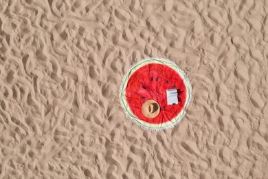 Towel with book and straw hat on sandy beach, aerial top view. Space for text