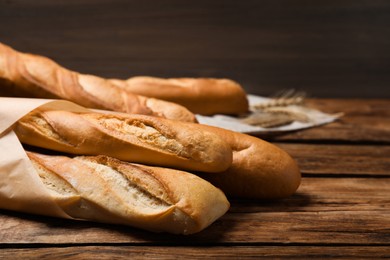 Photo of Fresh tasty baguettes and spikelets on wooden table, closeup