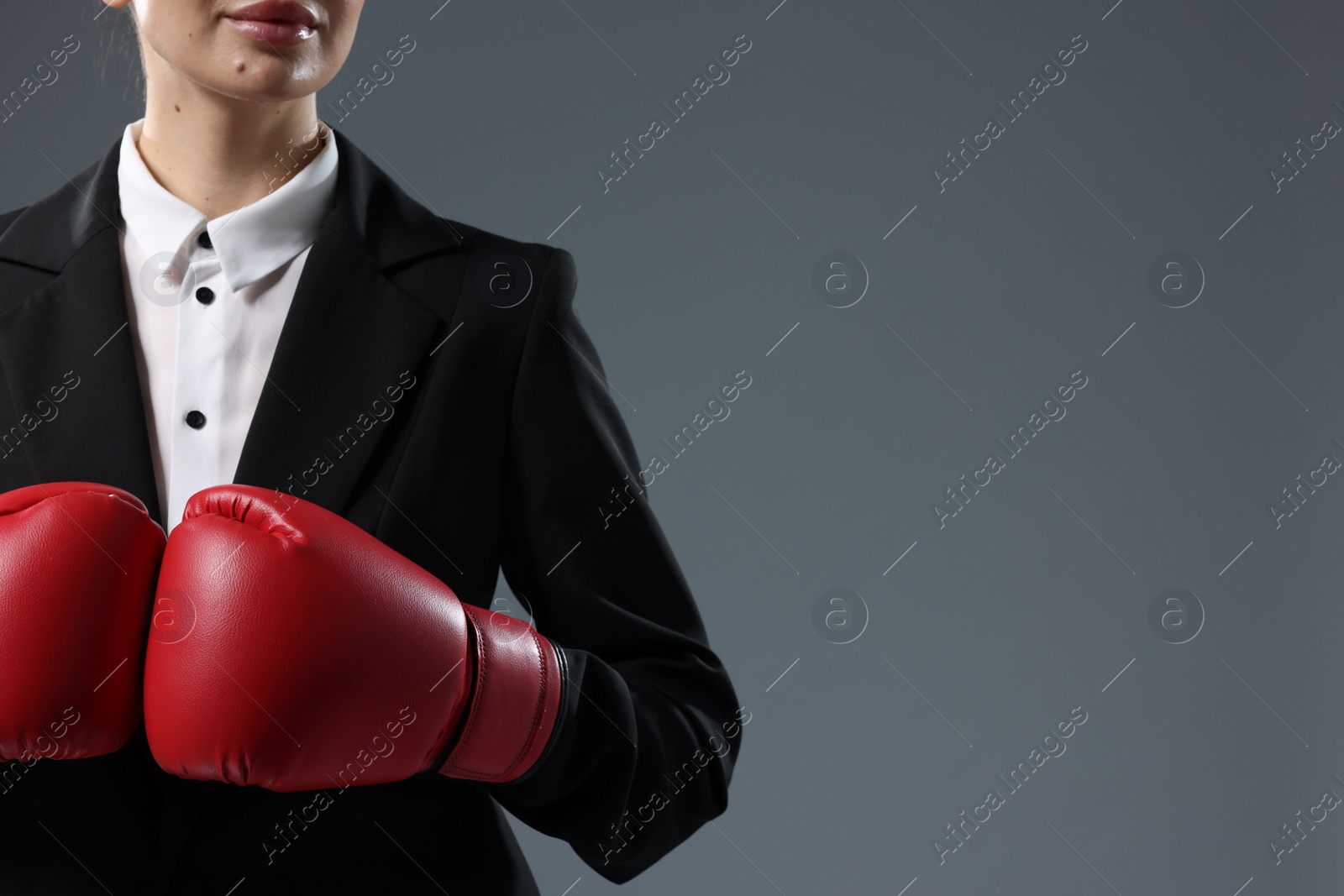 Photo of Businesswoman in suit wearing boxing gloves on grey background, closeup. Space for text