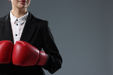 Businesswoman in suit wearing boxing gloves on grey background, closeup. Space for text