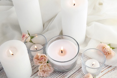 Photo of Composition with burning aromatic candles and roses on wooden table