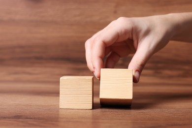 Woman arranging cubes on wooden background, closeup. Idea concept
