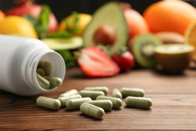 Photo of Vitamin pills, bottle and fruits on wooden table. Space for text