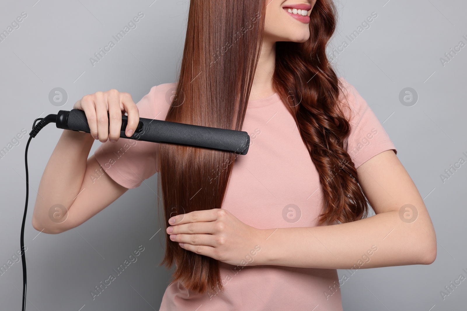 Photo of Young woman using hair iron on light gray background, closeup