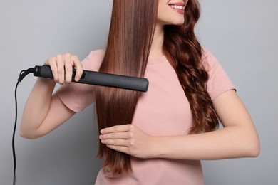 Photo of Young woman using hair iron on light gray background, closeup