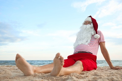 Photo of Santa Claus relaxing on beach, space for text. Christmas vacation