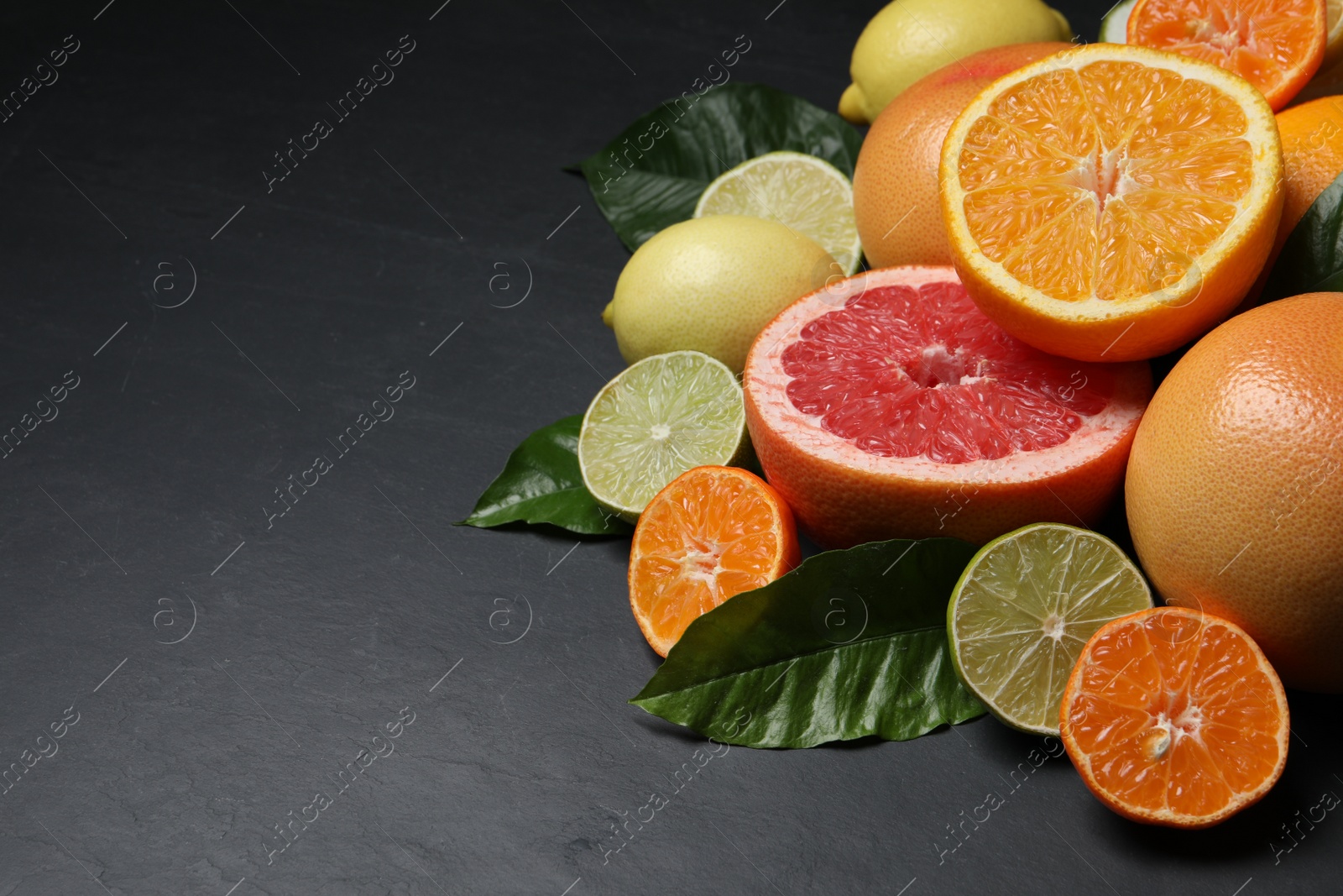 Photo of Different ripe citrus fruits with green leaves on black table. Space for text