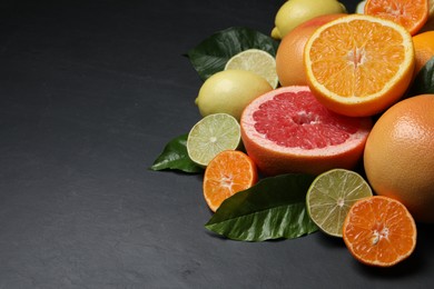 Photo of Different ripe citrus fruits with green leaves on black table. Space for text