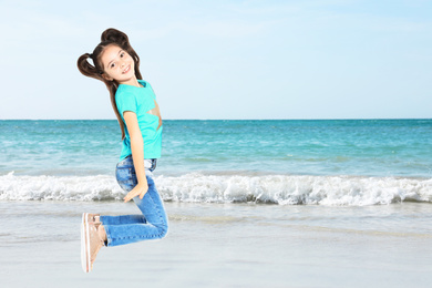 Happy school girl jumping on beach near sea, space for text. Summer holidays