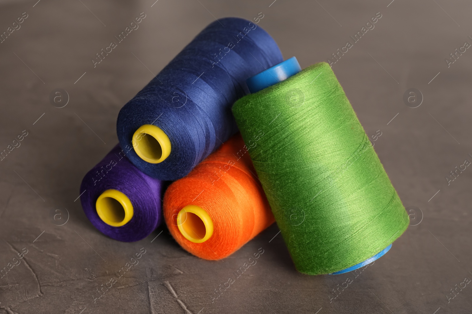 Photo of Set of color sewing threads on grey table, closeup