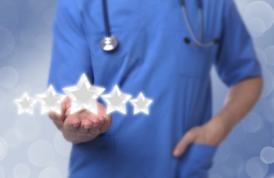 Quality rating. Doctor with stethoscope holding virtual stars against light blue background, closeup