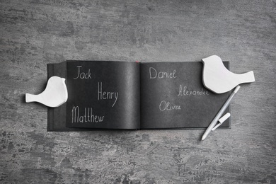 Notebook with different baby names, pen and bird shaped figures on grey table, flat lay