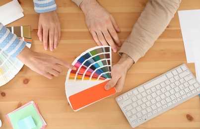 Photo of Designers with paint color palette samples at table, top view