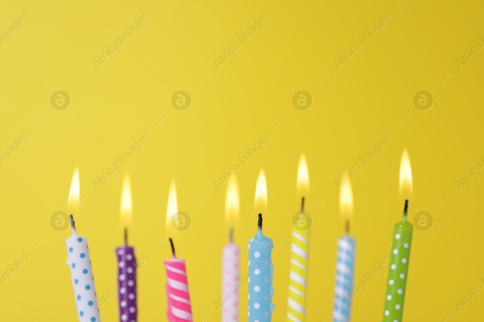 Photo of Many burning candles on yellow background, closeup. Birthday celebration