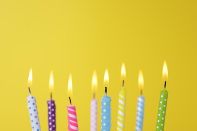 Photo of Many burning candles on yellow background, closeup. Birthday celebration