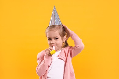 Photo of Birthday celebration. Cute little girl in party hat with blower on orange background