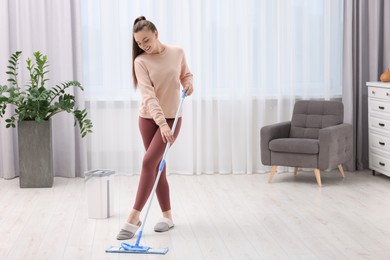 Photo of Happy woman mopping floor at home. Space for text