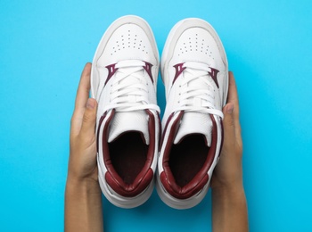 Photo of Woman holding pair of stylish shoes on blue background, top view