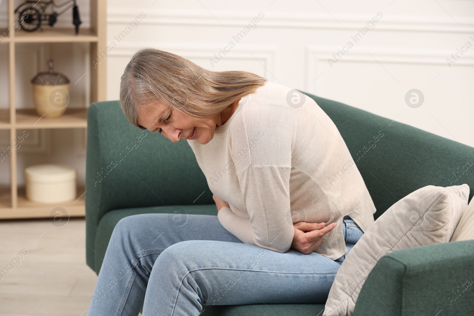 Photo of Menopause. Woman suffering from abdominal pain on sofa at home