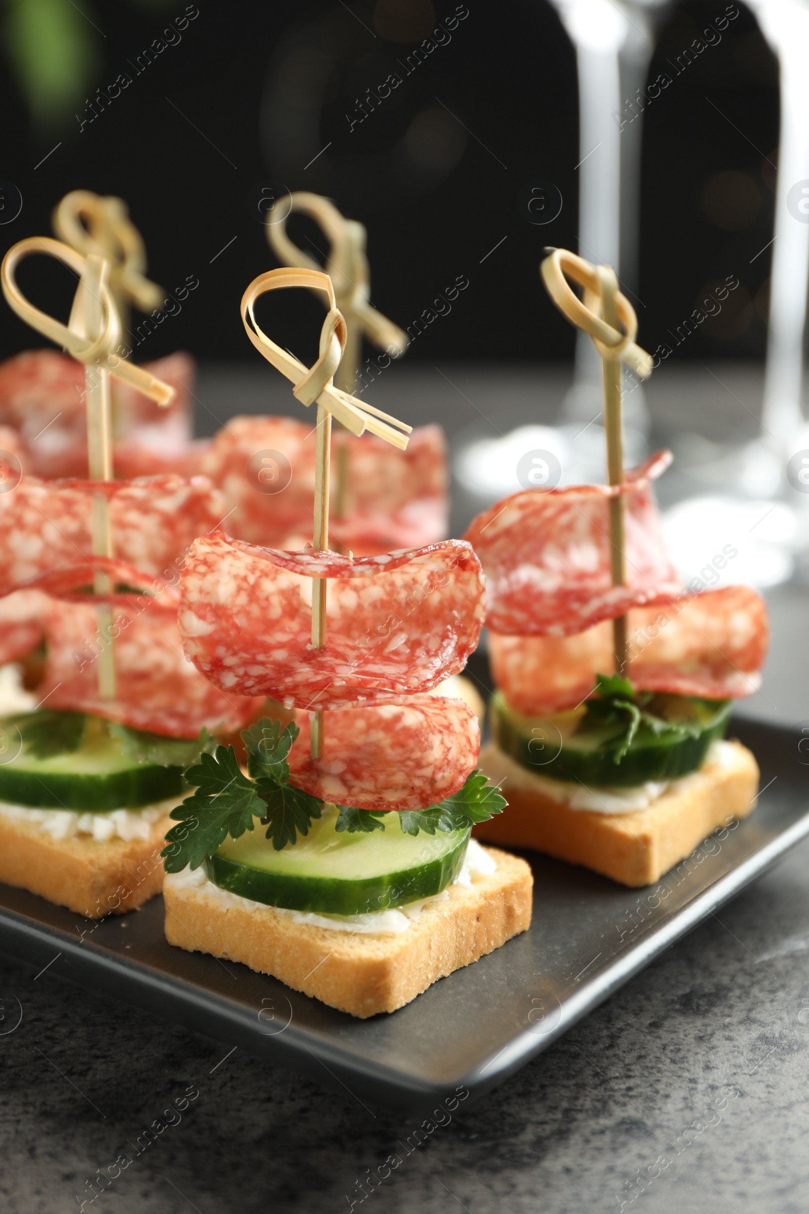 Photo of Tasty canapes with salami, cucumber and cream cheese on grey table, closeup