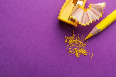 Photo of Yellow pencil, shaving, crumbs and sharpener on purple background, flat lay. Space for text
