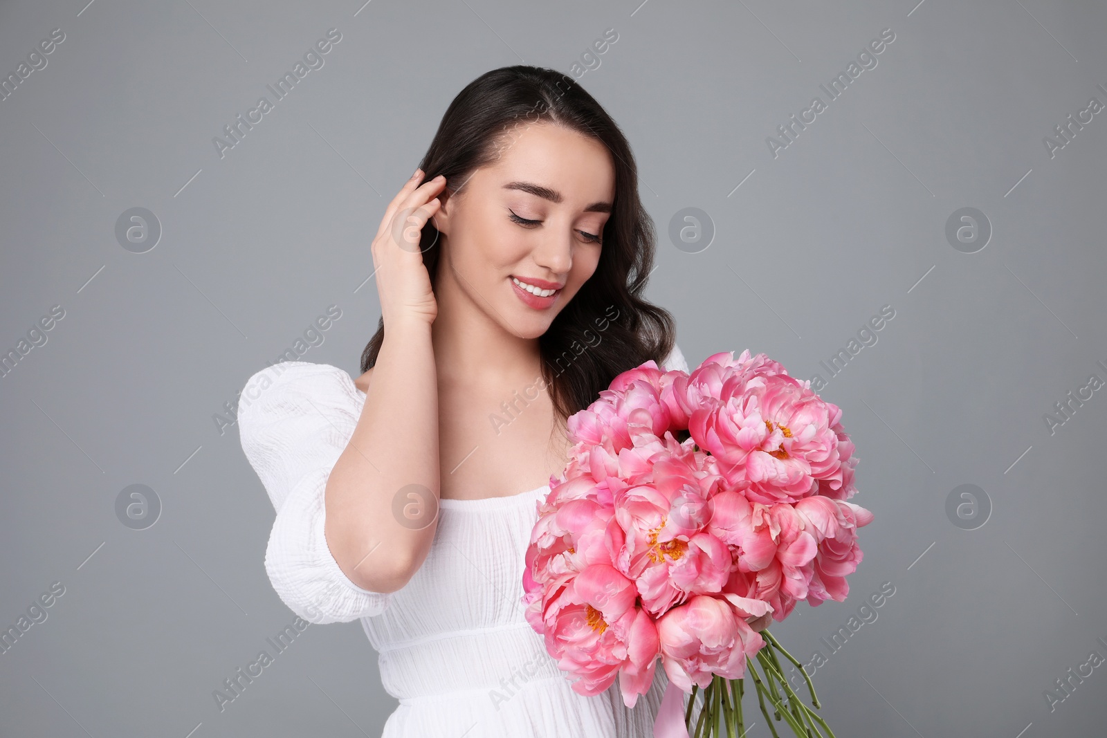 Photo of Beautiful young woman with bouquet of pink peonies on grey background