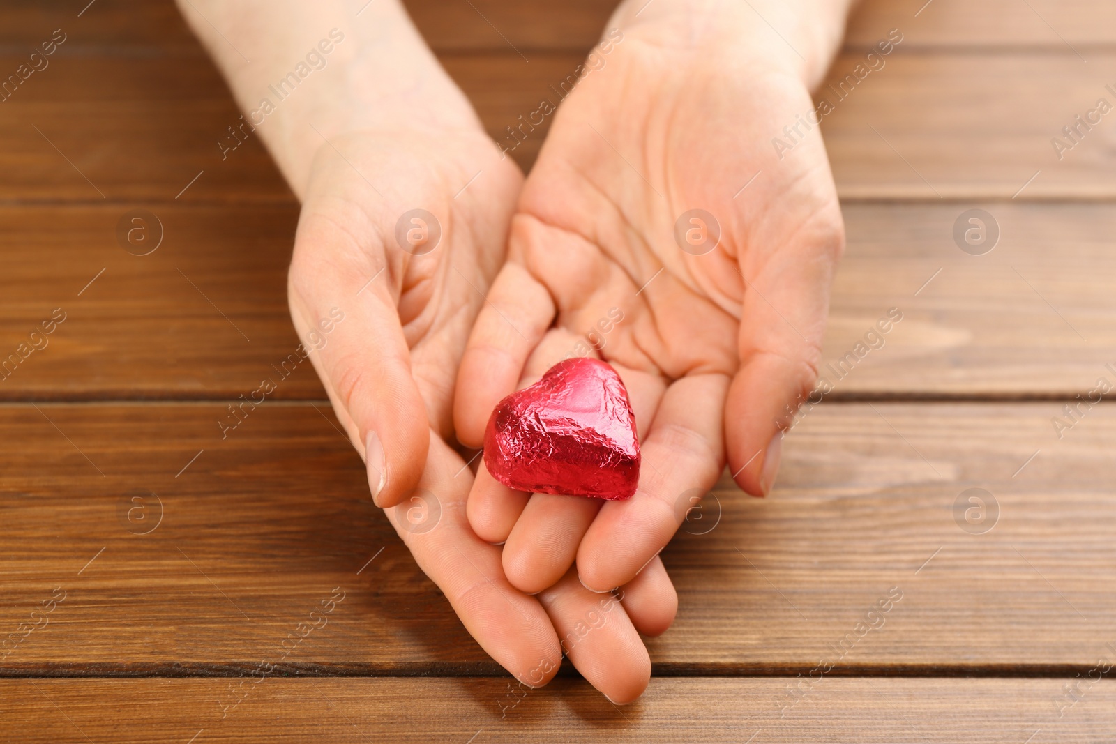 Photo of Woman holding heart shaped chocolate candy at wooden table, closeup