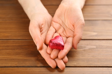 Photo of Woman holding heart shaped chocolate candy at wooden table, closeup