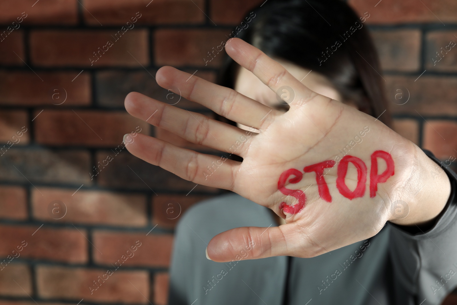 Photo of Domestic violence concept. Unhappy woman hiding her face, focus on hand with written word Stop