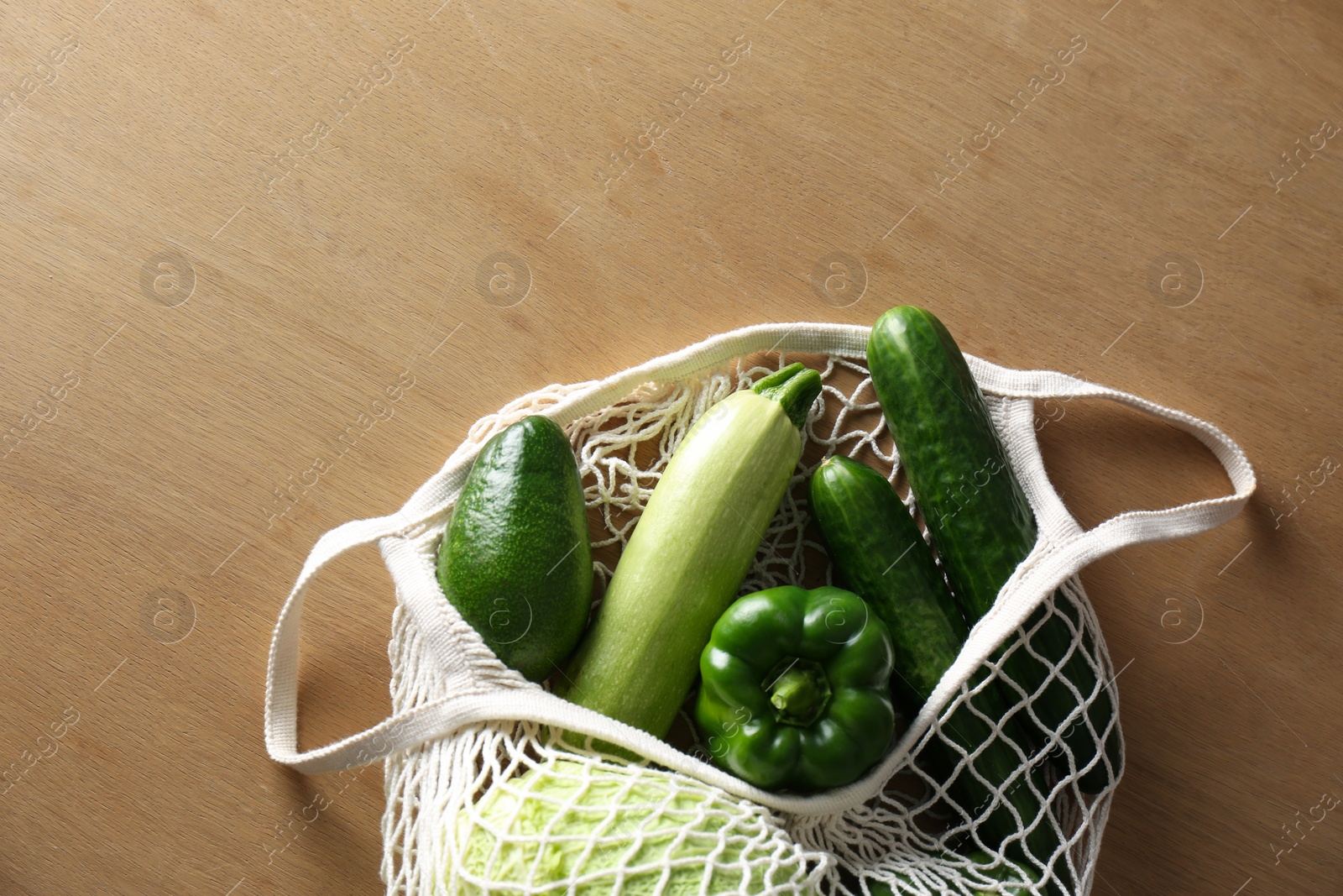 Photo of Different fresh vegetables in eco mesh bag on wooden table, top view