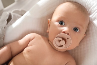 Cute little baby with pacifier lying in crib, top view