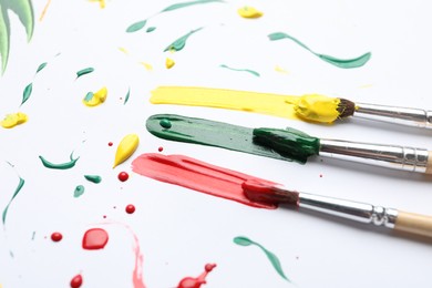 Photo of Brushes with different paints and strokes on white background, closeup